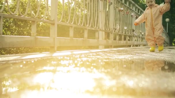 Lycklig bebis flicka i orange vattentät regnrock och gummi regn stövlar gå på pölar efter regn, slow motion shot — Stockvideo