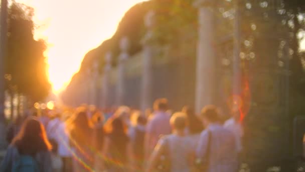 Neznámí lidé v příležitostných šatech při letním západu slunce. Přeplněný chodník poblíž městského parku, pomalý pohyb — Stock video
