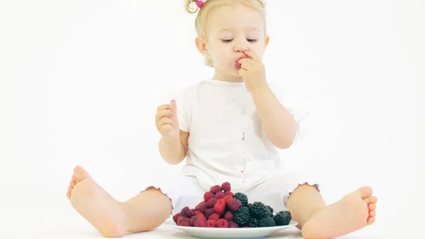 Söt blond Baby Girl äter bär mot vit bakgrund — Stockfoto