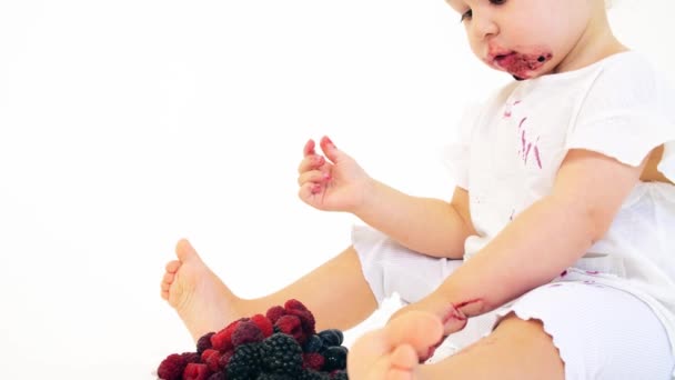 Funny baby girl eats berries against white background — Stock Video