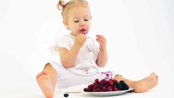 Adorable baby girl eating fresh juicy berries on white background — Stock Video