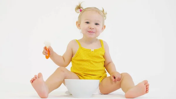 Mutlu sarışın bebek kız beyaz arka plan karşı onu yulaf ezmesi yiyor — Stok fotoğraf