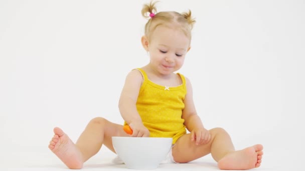 Boldog szőke kislány eszik neki zabpehely ellen, fehér háttér — Stock videók