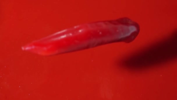 Shora dolů pohled na červený horký pepř, který padá na červenou rajčatovou šťávu nebo omáčku, super pomalý pohyb — Stock video