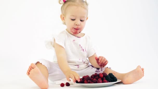 Smudged baby girl eats berries against white background — Stock Video