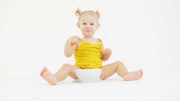 Vrolijke baby meisje eet haar maaltijd op witte achtergrond — Stockvideo