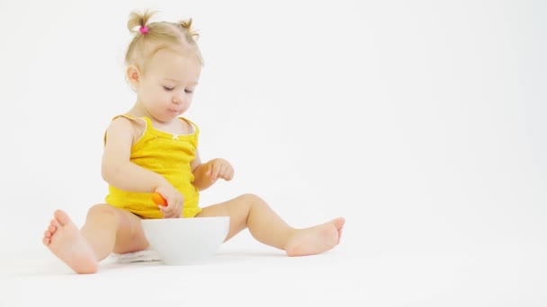 Blonde baby girl eats her breakfast on white background — Stock Video