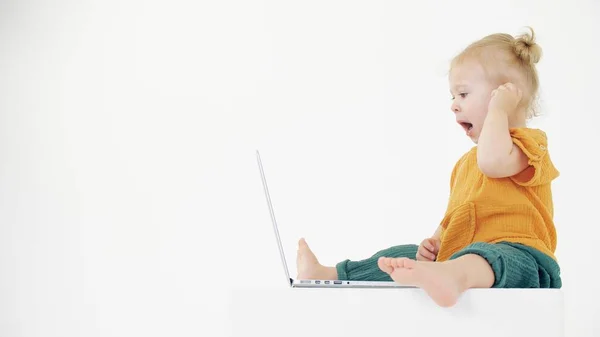 Yawning baby girl looks at the laptop screen on white background. Boring content related clip — Stock Photo, Image