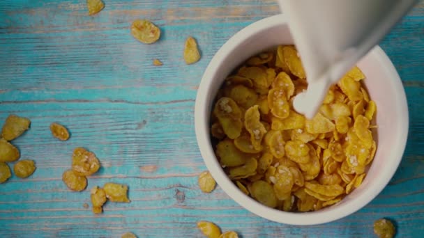 Aggiunta di latte ai corn flakes sul tavolo di legno blu, top down super slow motion shot — Video Stock