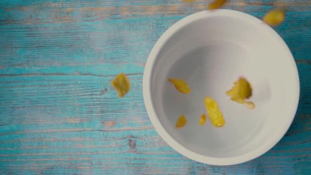 Падаючі кукурудзяні пластівці і миска на синьому дерев'яному столі, супер повільний рух — стокове відео