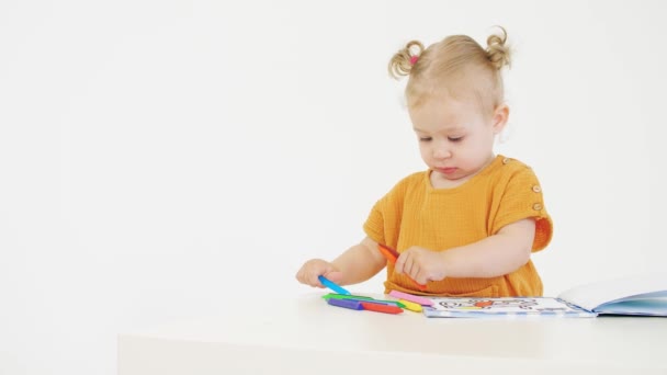 Baby girl coloring unrecognizable picture with crayons on white background — Stock Video