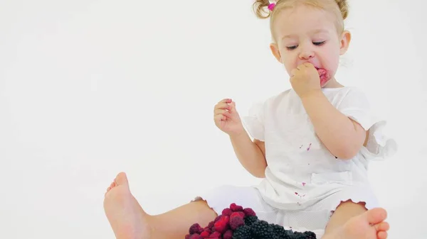 Bebê menina come framboesas frescas e amoras contra fundo branco — Fotografia de Stock