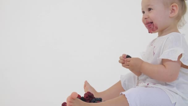Gelukkig baby meisje eet sappige bessen op lichte achtergrond — Stockvideo