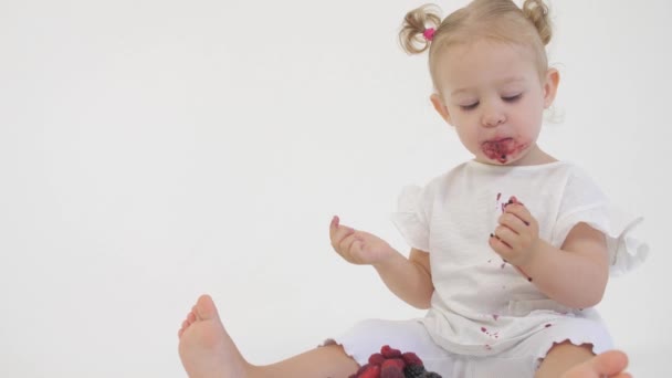 Cute baby eats juicy raspberries and blackberries against light background — Stock Video