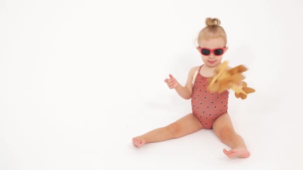 Baby girl wearing swimsuit and sunglasses plays with generic wooden plane. Vacation related clip — Stock Video