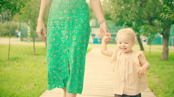 Usmívající se holčička a její matka chodí po cestě parkem — Stock fotografie