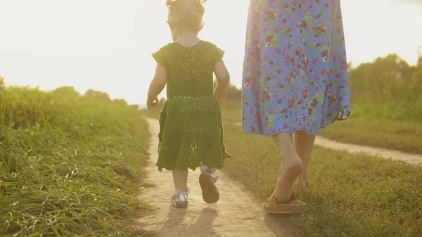 Bebê menina e sua mãe caminham juntos ao longo do caminho de campo rural em um dia ensolarado — Fotografia de Stock