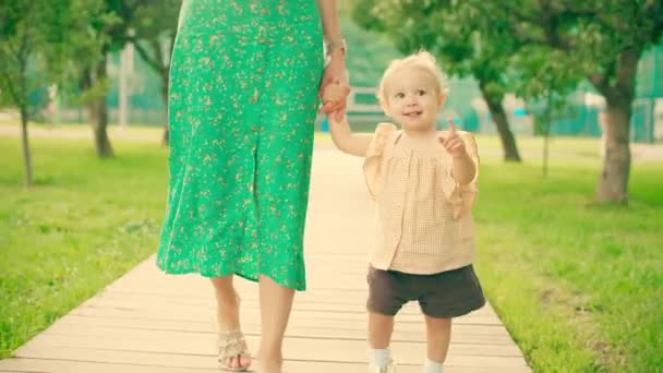Улыбающаяся малышка и ее мама идут по дорожке парка — стоковое видео