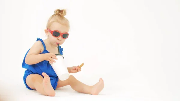 Menina loira usando óculos de sol come e bebe de xícara de papel com uma palha — Fotografia de Stock