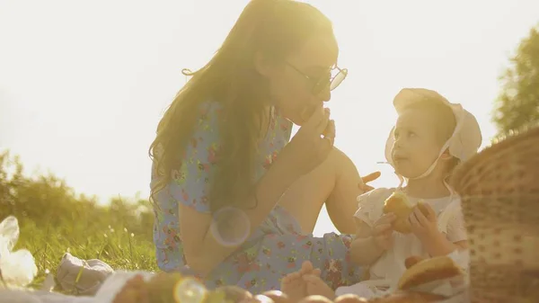 Bebê e mãe comem juntos ao ar livre. Fazer piquenique em um dia quente de verão — Fotografia de Stock