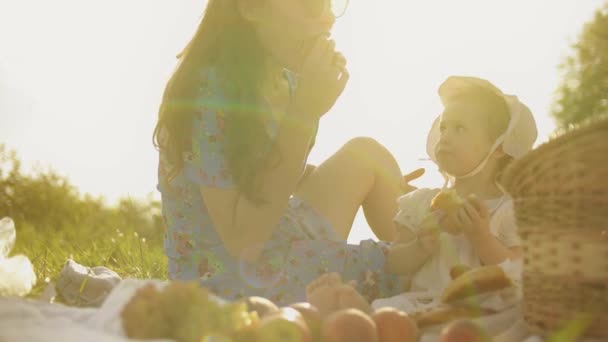 Bebé y mamá comen juntos al aire libre. Hacer picnic en un día caluroso de verano — Vídeos de Stock