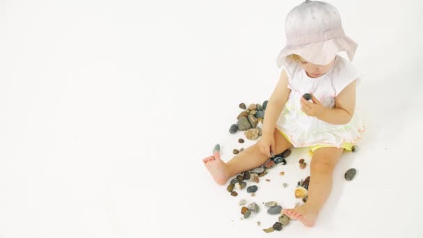 Niña con sombrero de cubo juega con guijarro de mar y conchas sobre fondo blanco. Clip relacionado con vacaciones — Vídeos de Stock