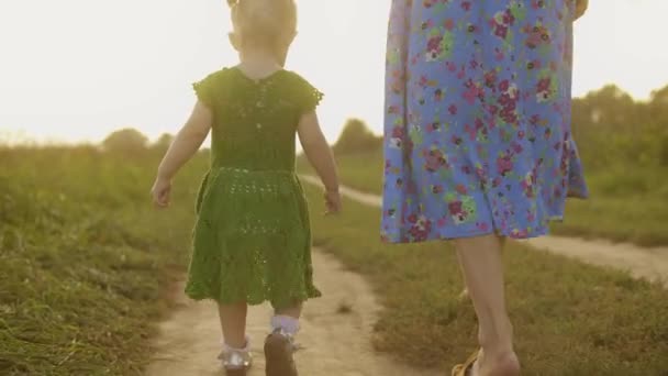 Baby girl in green dress and her mum walk along rural field pathway together on a sunny summer evening — Stock Video
