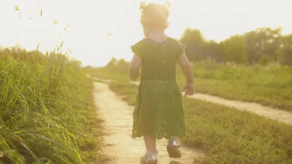 Baby girl wearing green dress walks along the path on a hot sunny summer evening — Φωτογραφία Αρχείου