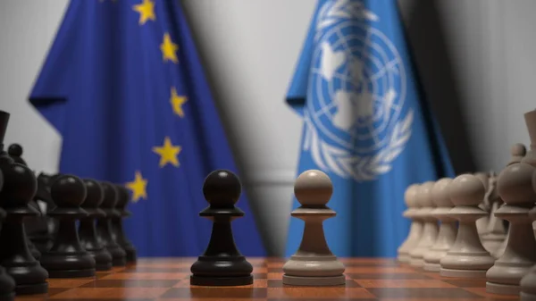 Drapeaux de l'UE et des Nations unies derrière des pions sur l'échiquier. Jeu d'échecs ou rivalité politique liée au rendu 3D — Photo