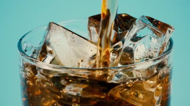 Nalít colu nebo hnědý nealkoholický nápoj do sklenice plné kostek ledu na azurovém pozadí, detailní pomalý záběr na červenou — Stock video