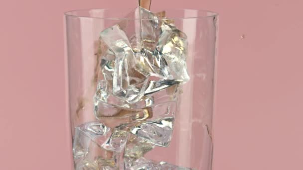 Verter refresco marrón en un vaso lleno de cubitos de hielo sobre fondo rosa, primer plano de cámara lenta sobre rojo — Vídeos de Stock