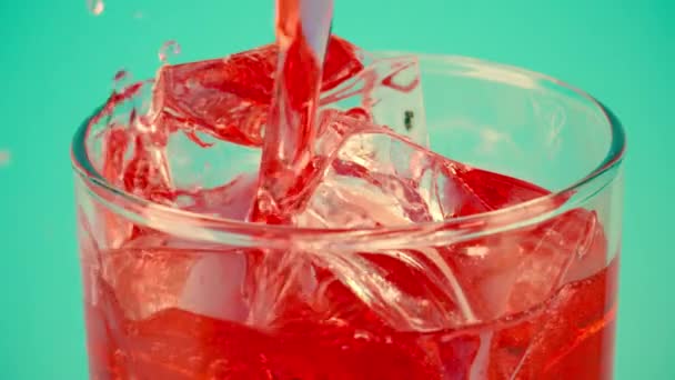 Derramando refrigerante vermelho em um copo cheio de cubos de gelo contra o fundo ciano, close-up tiro em câmera lenta no vermelho — Vídeo de Stock