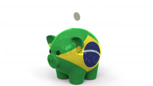 As moedas caem no banco piggy pintado com a bandeira do Brasil. Sistema bancário nacional ou animação conceitual 3D relacionada com poupança — Vídeo de Stock