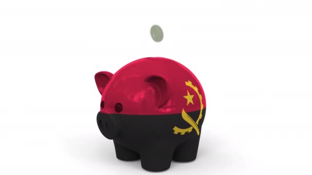 As moedas caem no banco piggy pintado com a bandeira de Angola. Sistema bancário nacional ou animação conceitual 3D relacionada com poupança — Vídeo de Stock