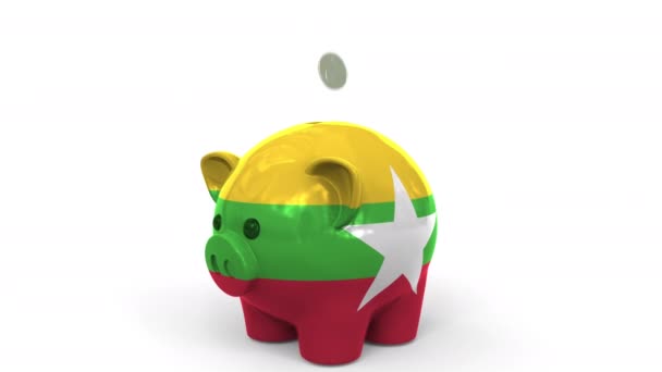 Монеты попадают в копилку, раскрашенную флагом Мьянмы. Национальная банковская система или связанная с ней концептуальная 3D анимация — стоковое видео