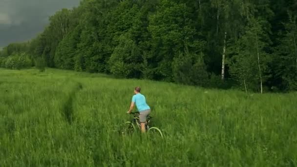 Повітряний знімок невідомого молодого чоловіка, що їде на велосипеді вздовж зеленого лугу — стокове відео