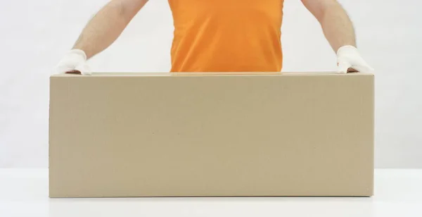 O funcionário do armazém em uniforme laranja coloca uma grande caixa de papelão na mesa. 6K vídeo filmado no vermelho — Fotografia de Stock