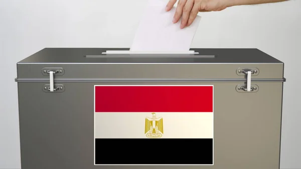Hand legt Stimmzettel in die Wahlurne mit der Flagge Ägyptens. Wahlbezogene 3D-Darstellung — Stockfoto