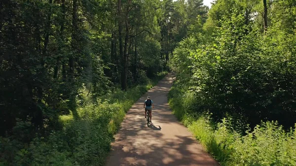 Aerial seguinte tiro de um ciclista movendo-se ao longo de uma estrada ensolarada parque de verão — Fotografia de Stock