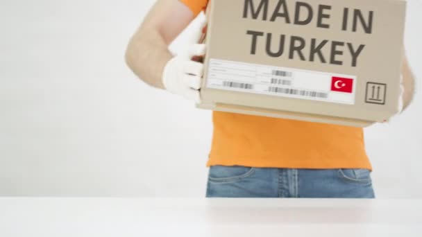 Trabalhador vestindo uniforme laranja coloca caixa com MADE IN TURKEY imprimir na mesa — Vídeo de Stock