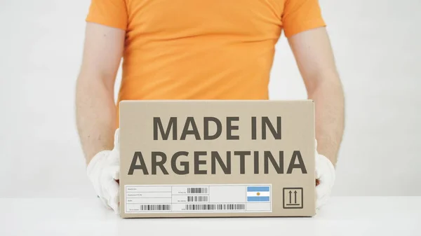 El hombre pone una caja de cartón con texto MADE IN ARGENTINA sobre la mesa —  Fotos de Stock