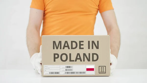 El hombre pone una caja de cartón con texto MADE IN POLAND sobre la mesa —  Fotos de Stock