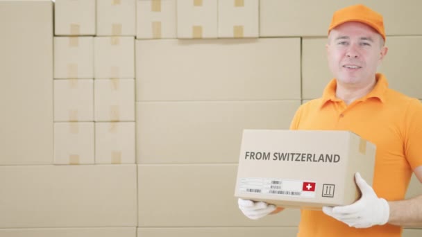 Hombre sosteniendo un paquete de cartón con texto impreso DE SUIZA en él — Vídeo de stock