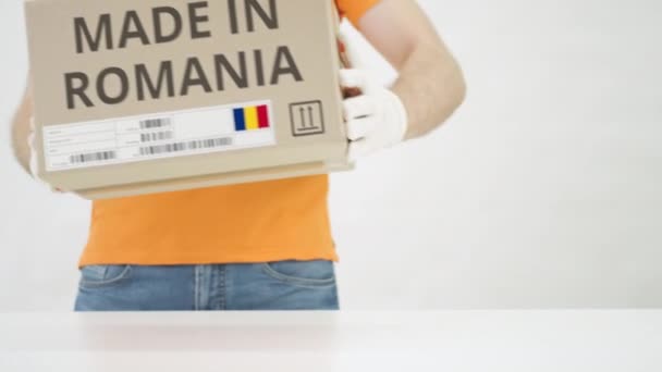 Pracovník v oranžové uniformě dává na stůl krabici s potiskem MADE IN ROMANIA — Stock video