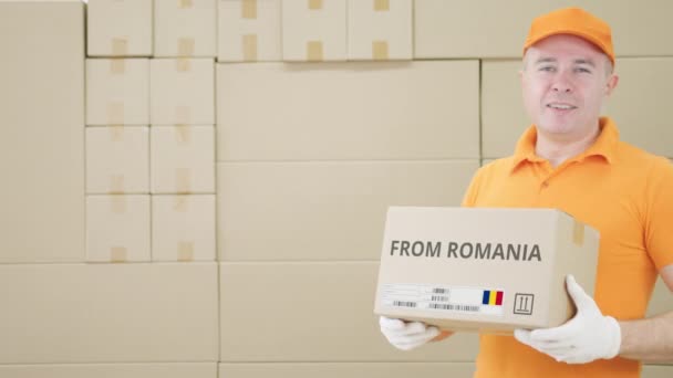 Warehouse worker holds cardboard box with printed FROM ROMANIA text on it — Stock Video