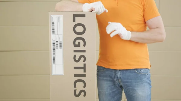 Trabalhador do armazém com grande parcela com texto LOGISTICS impresso e etiqueta nele — Fotografia de Stock