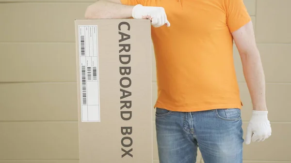 Carrying big carton with CARDBOARD BOX text against parcel stacks background — Stock Photo, Image