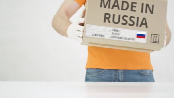 Man menempatkan kotak kardus dengan MADE IN teks RUSSIA di atas meja — Stok Video