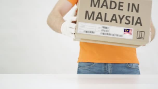 Muž položí kartónovou krabici s textem MADE IN MALAYSIA na stůl — Stock video