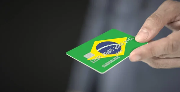 Man gives plastic bank card with printed flag of Brazil. Fictional numbers — Stock Photo, Image